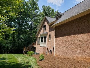 A large brick house with a lush green yard and trees in the background.