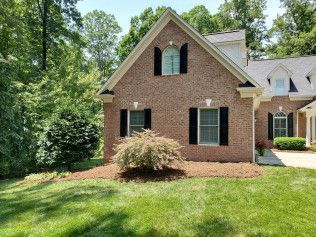 A brick house with black shutters and a lush green lawn in front of it.