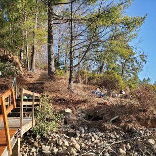 Wooded hillside with rocky shore and a wooden deck railing on the left under a clear blue sky