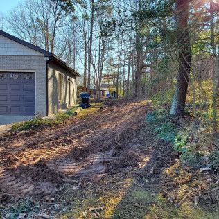 Mud-covered driveway beside a garage and woods, with tire tracks and a trash bin.