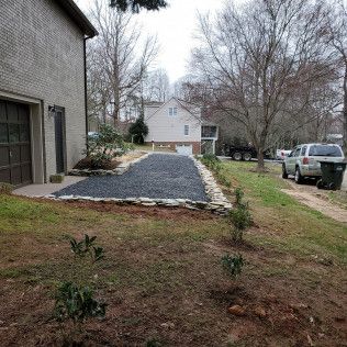 Gravel driveway beside a house, bordered by stones and shrubs, with a truck parked on the right.