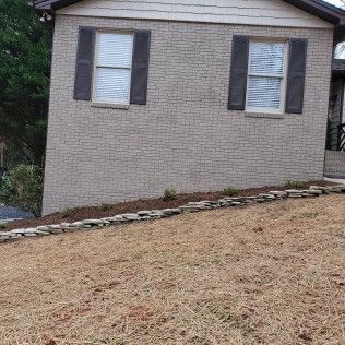 Side of a brick house with two windows, dark shutters, and a sloped dry lawn in front