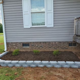 House exterior with gray siding, white window shutters, brick foundation, and a row of gray landscape stones.