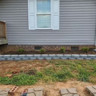 Backyard view of gray house siding, window with shutters, and a small landscaped bed with paver border