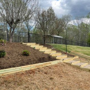 Backyard slope with wooden steps, black fence, and trees under a cloudy sky
