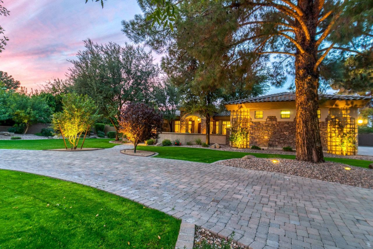 Well-lit house and stone driveway at dusk with green lawn and pink sky