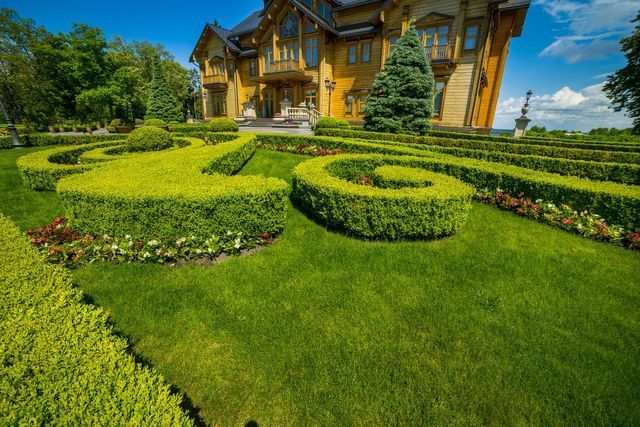 Yellow mansion with manicured topiary garden and bright green lawn under a blue sky