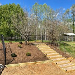 Wooden steps up a mulched garden slope with young plants and trees under a blue sky