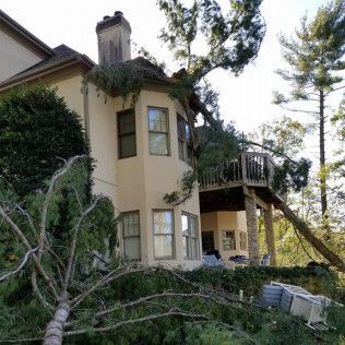 Tan house with balcony and fallen tree limbs in the foreground after storm damage