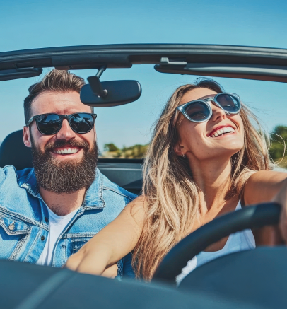 Two smiling people wearing sunglasses ride in a convertible under a blue sky.