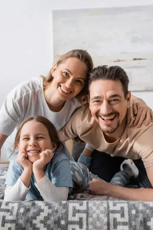 Smiling family of three lying on a couch, with parents hugging their child in a bright living room
