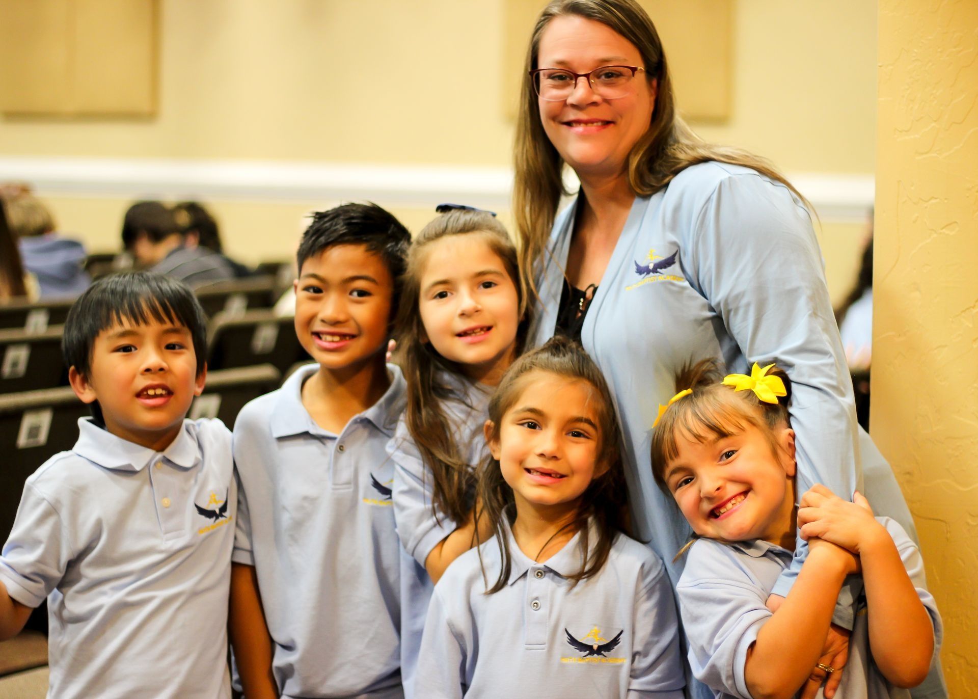 Teacher with five smiling children in matching gray uniforms indoors