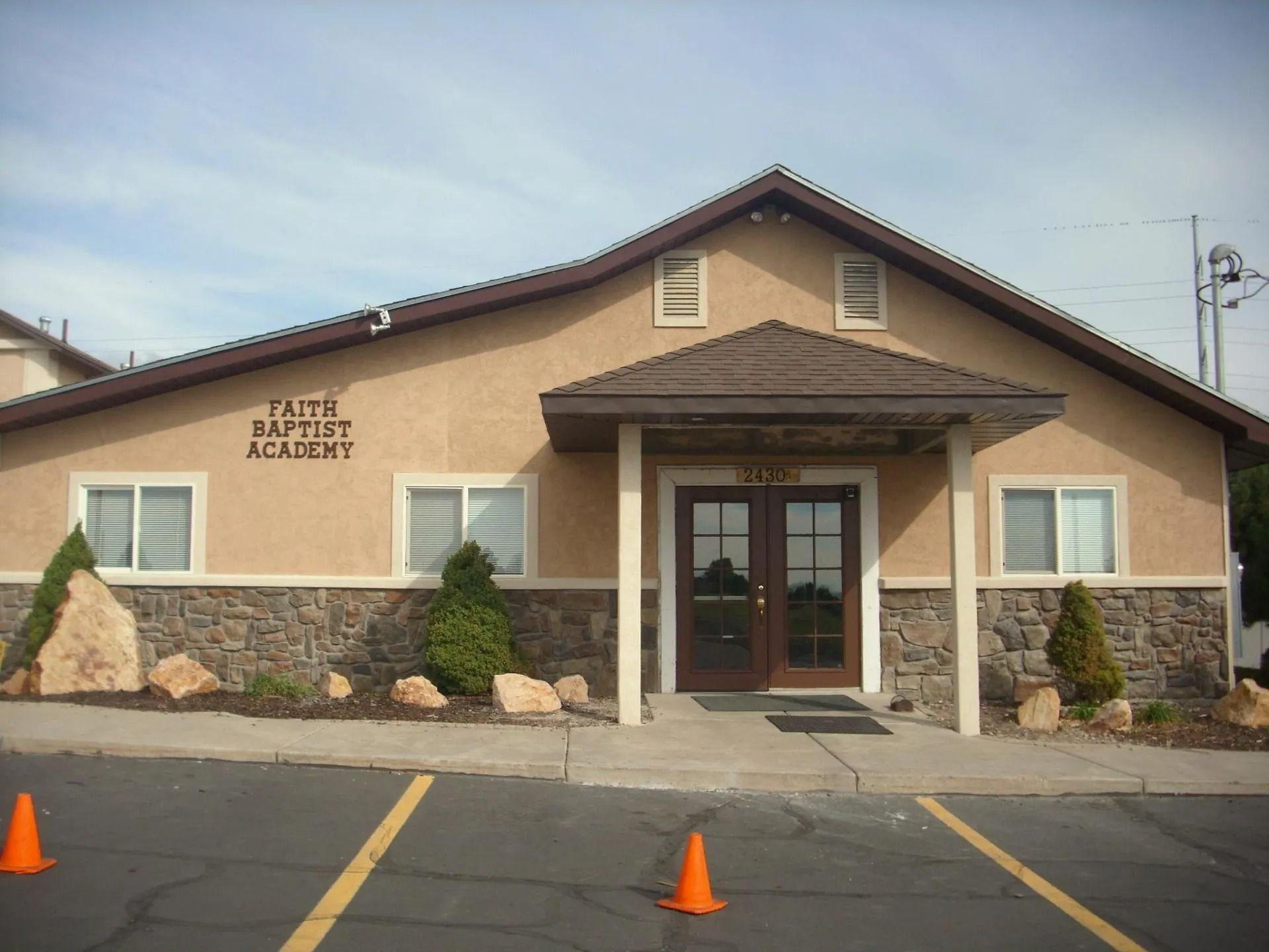 Baptist Academy building with stone facade and parking lot cones in front