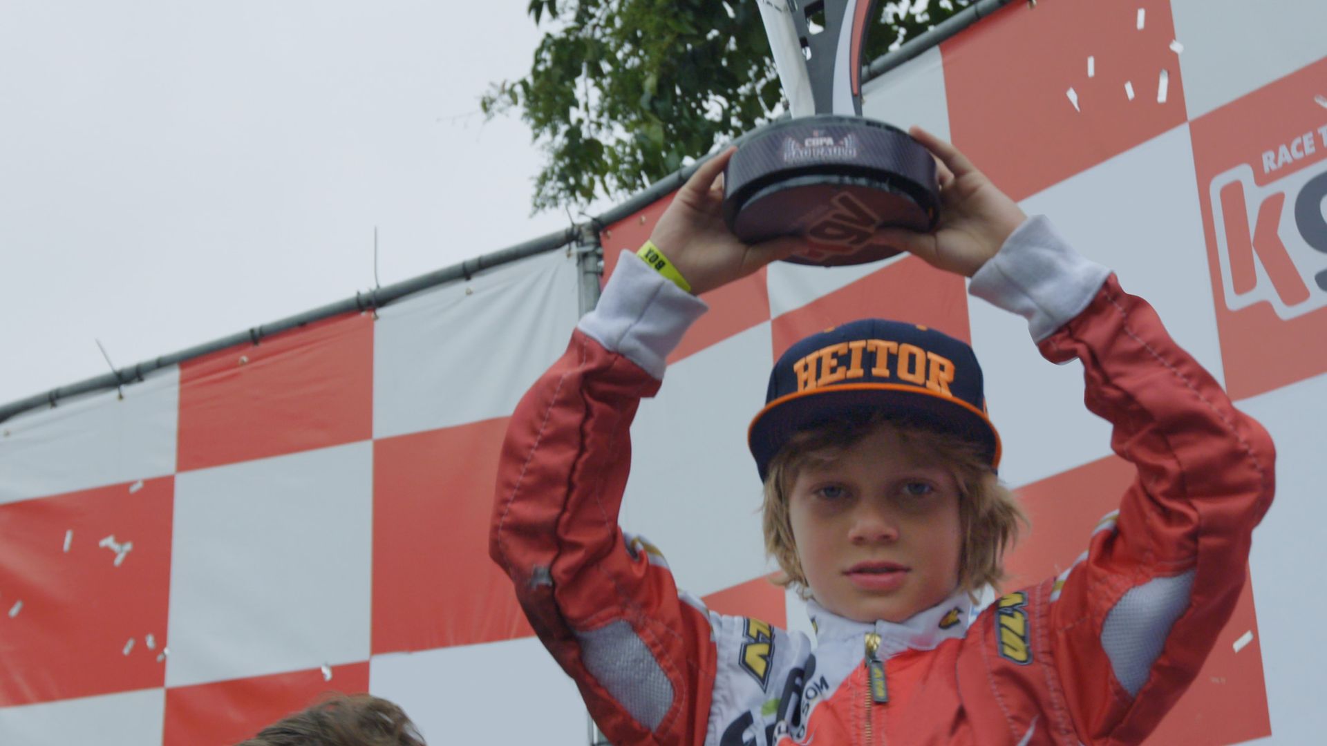A young boy in a heitor hat is holding a trophy over his head.