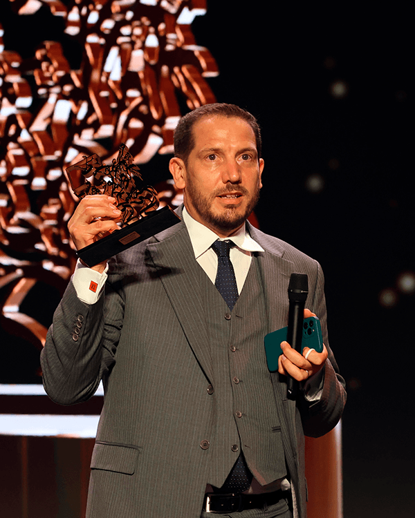 A man in a suit and tie is holding a microphone and a trophy.