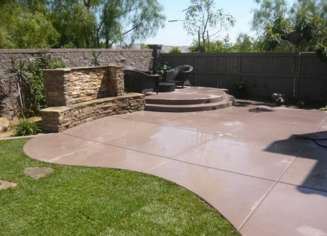 A backyard with a concrete patio and a stone wall.