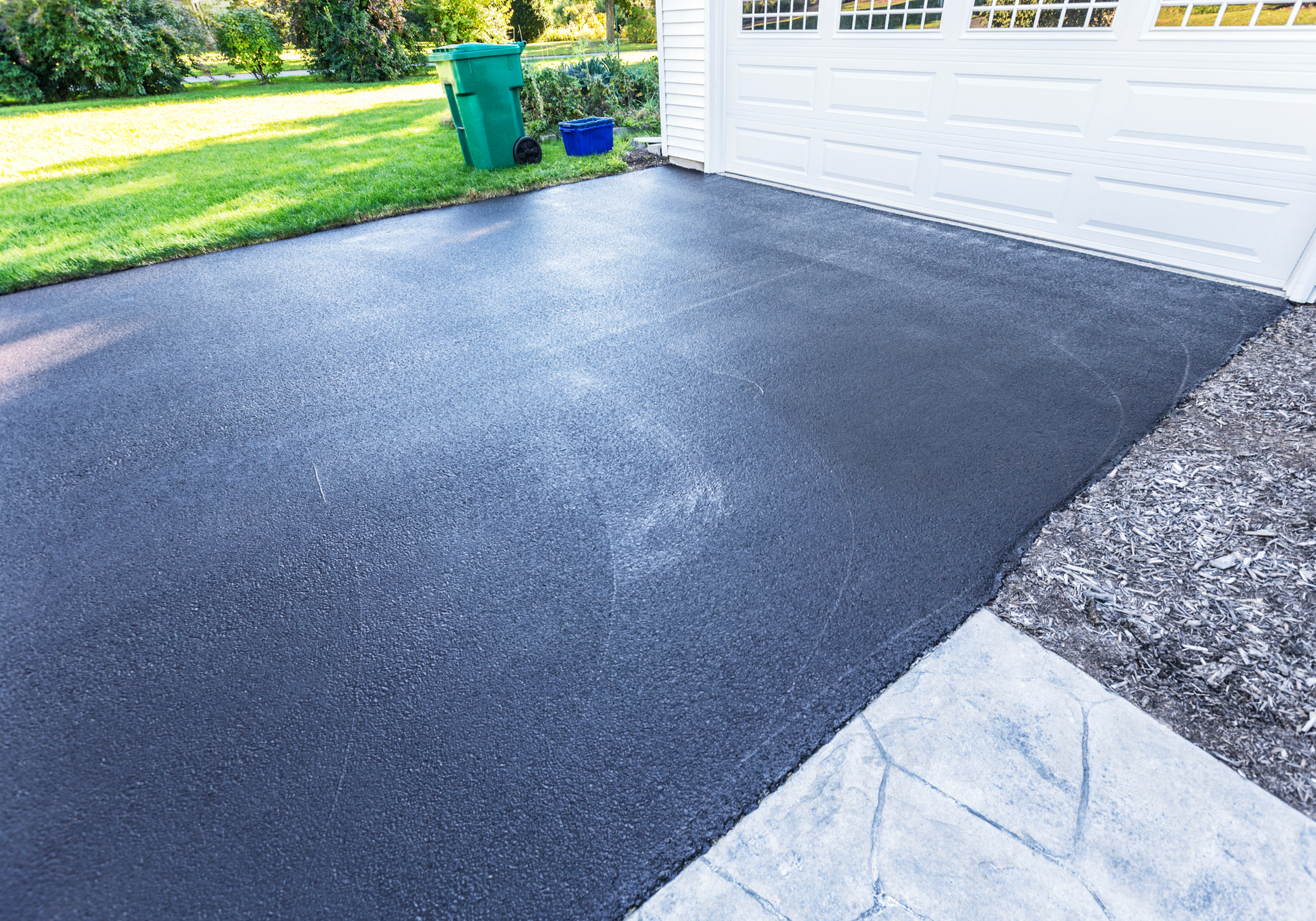 A black asphalt driveway next to a white garage door.