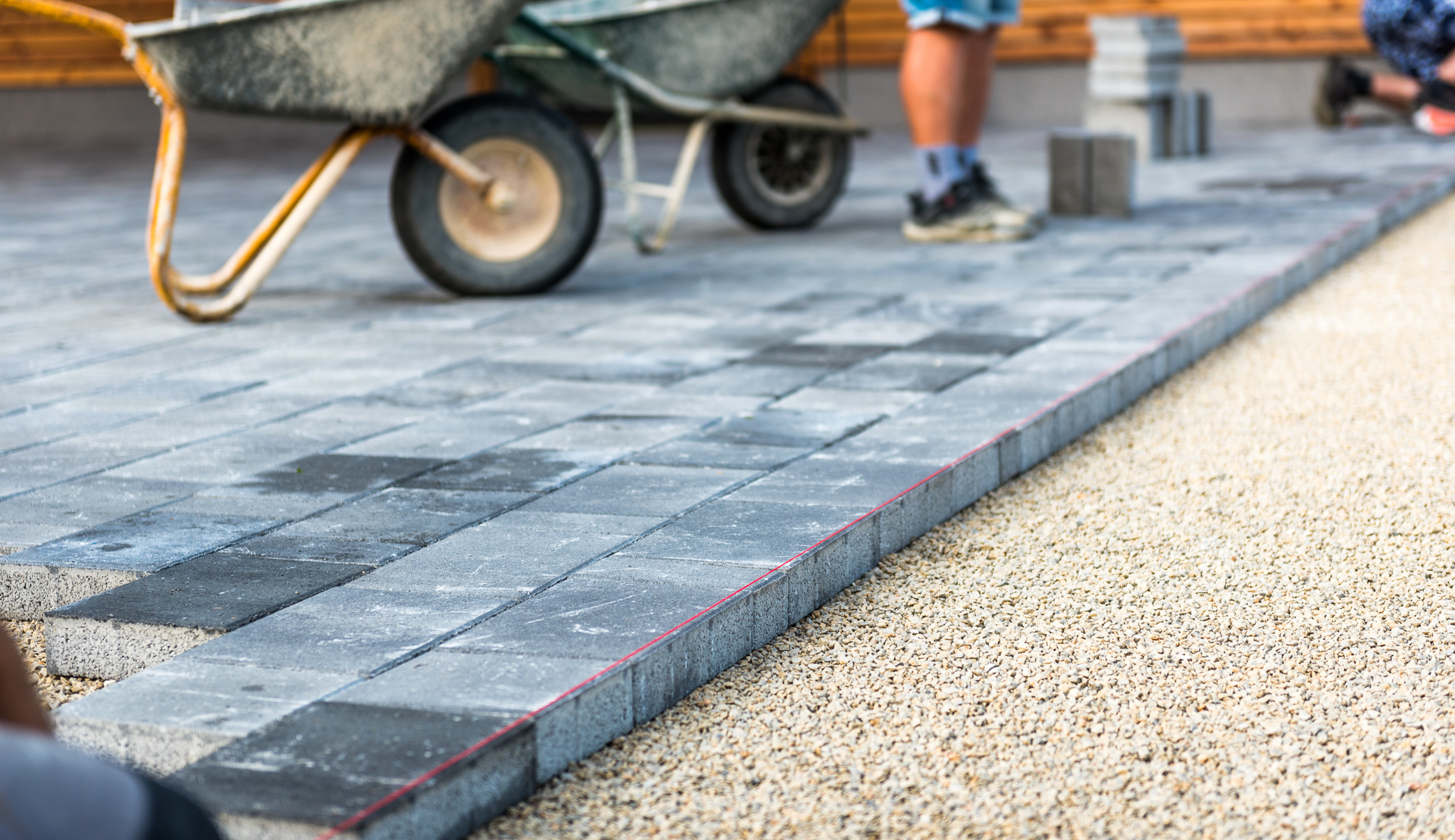 A wheelbarrow is being pushed down a brick driveway.