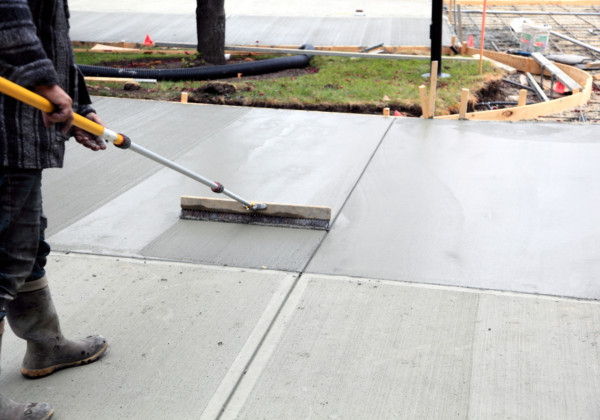 A man is using a broom to spread concrete on a sidewalk