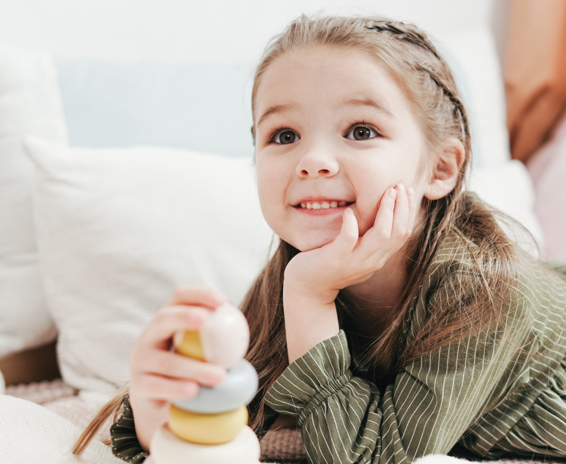 Child lying on a white bed, smiling and stacking colorful rings on a toy tower