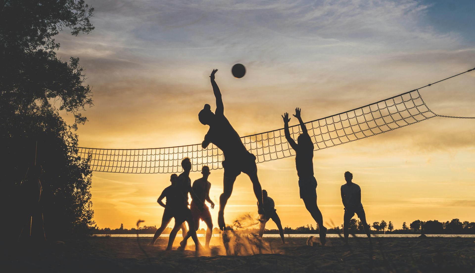 A group of athletes playing volleyball as the sun sets