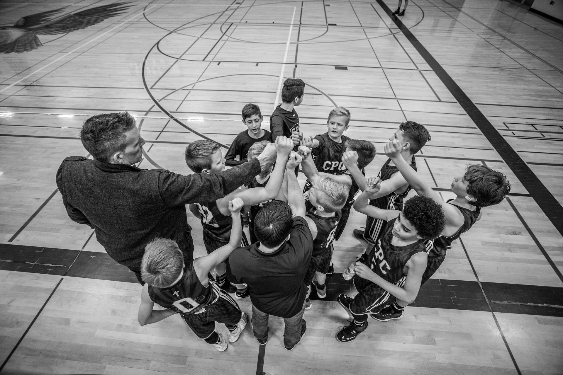 A group of basketball players huddled around their coach with their hands up, getting ready for a game