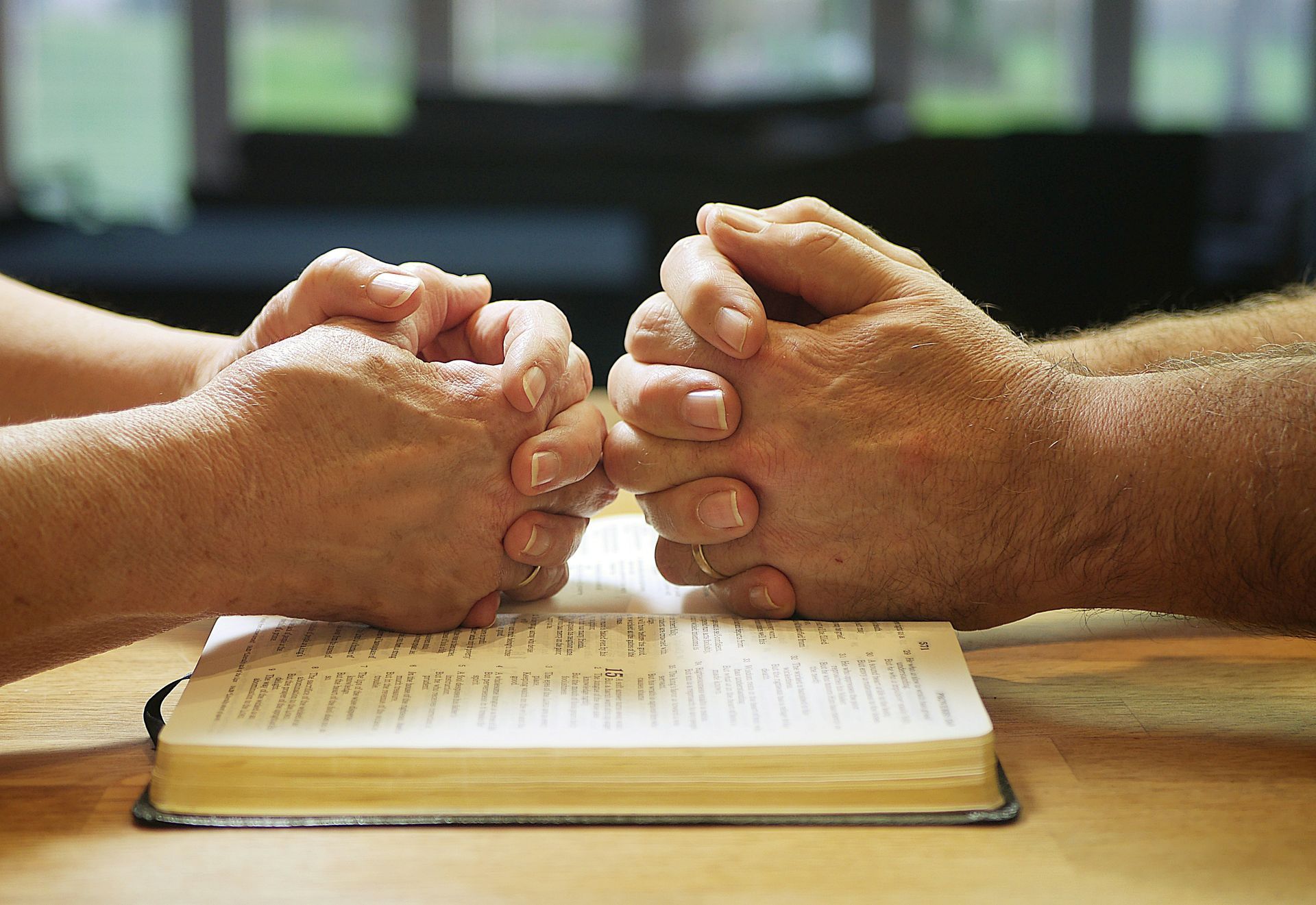 Two people's hands folded in prayer over a Bible