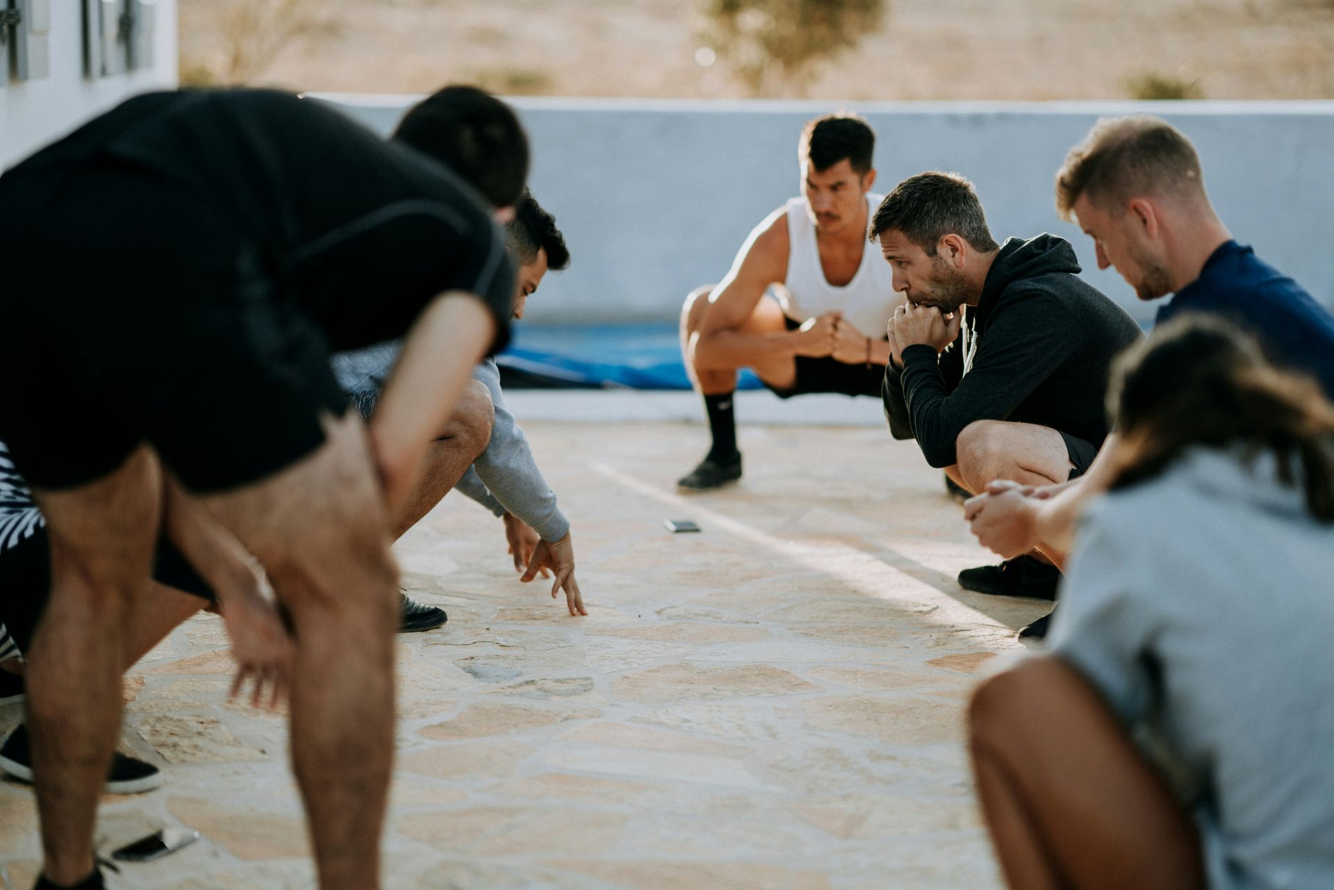 A group of leaders are squatting on the ground, learning from another leader who is teaching them