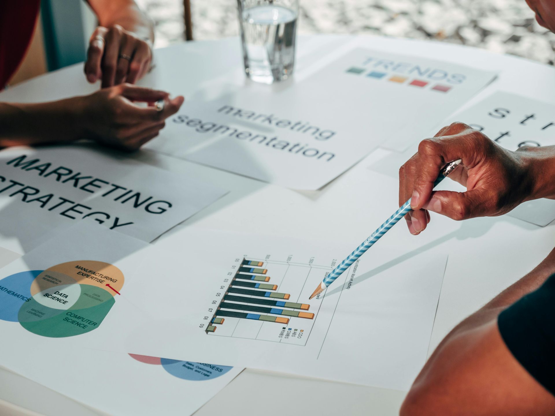 Hands pointing at charts on a table, reviewing marketing strategy and trends.