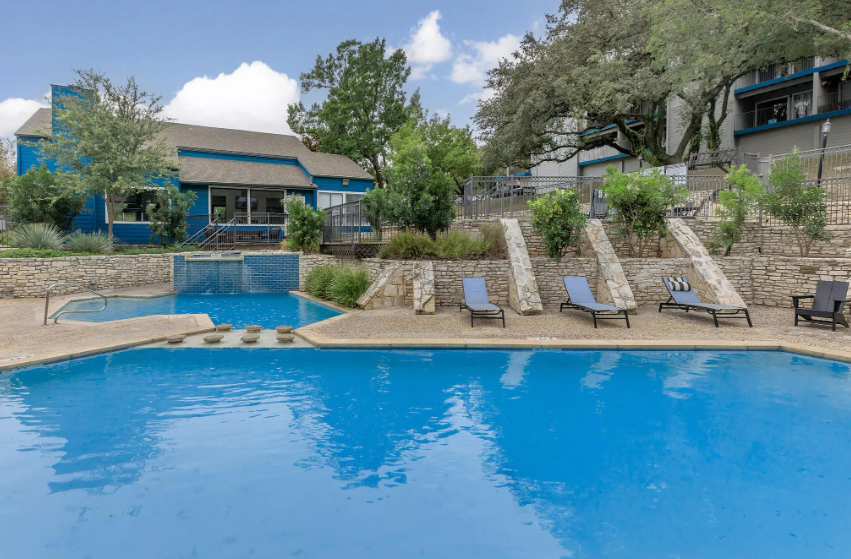 Resort pool with blue water, lounge chairs, stone waterfall, and buildings in the background