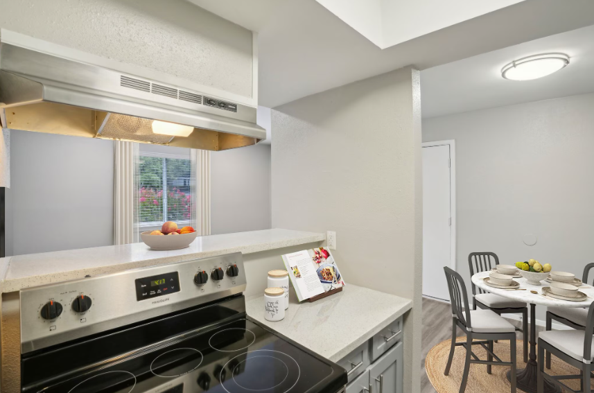 Bright kitchen with white appliances, a small dining table, and a window over the stove