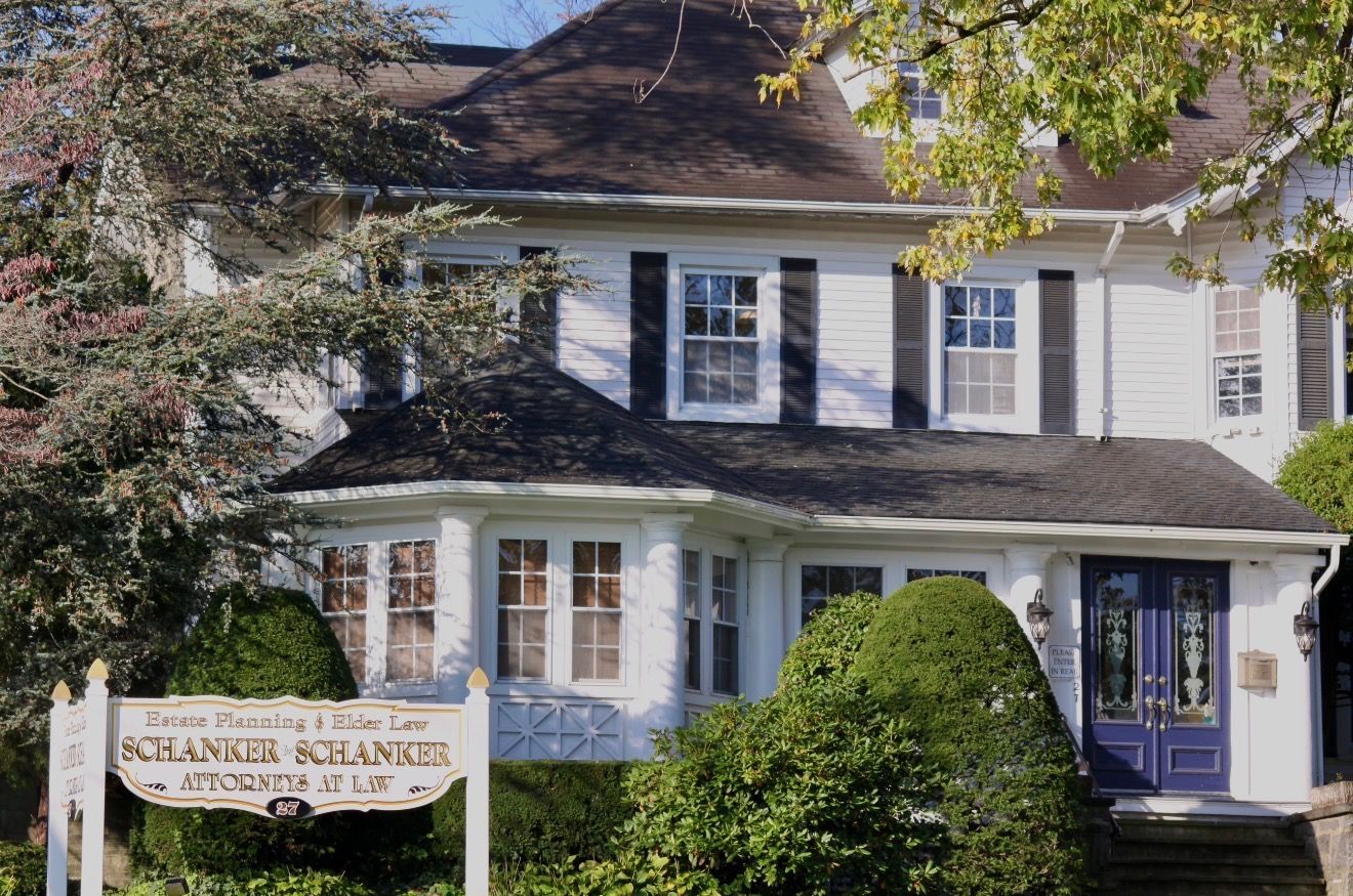 White two-story house with blue shutters and a sign reading “Stamford Alliance” by the front porch
