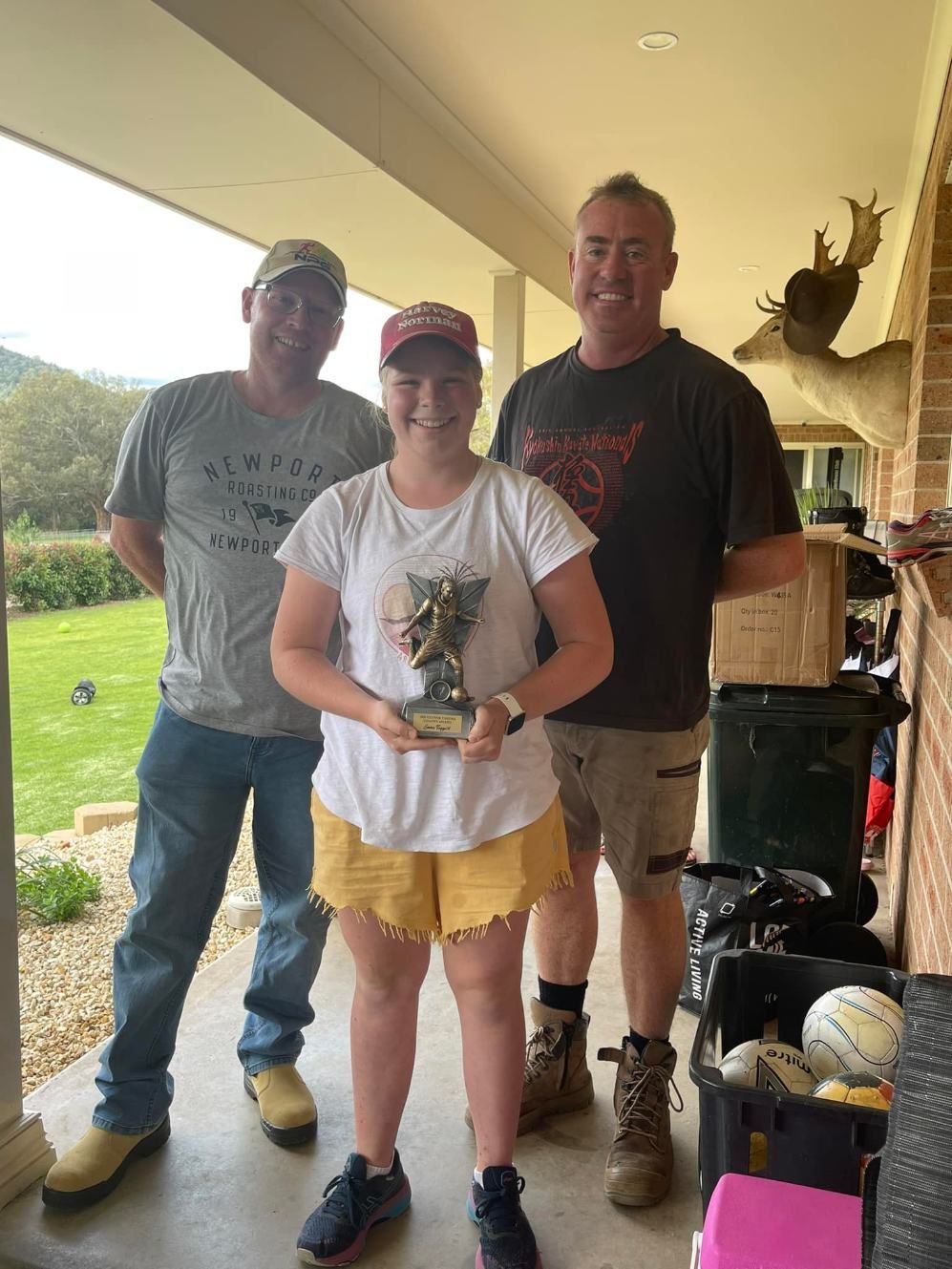 A Woman Is Holding A Trophy While Standing Next To Two Men On A Porch — Caterpillar Tree Services In Daruka, NSW