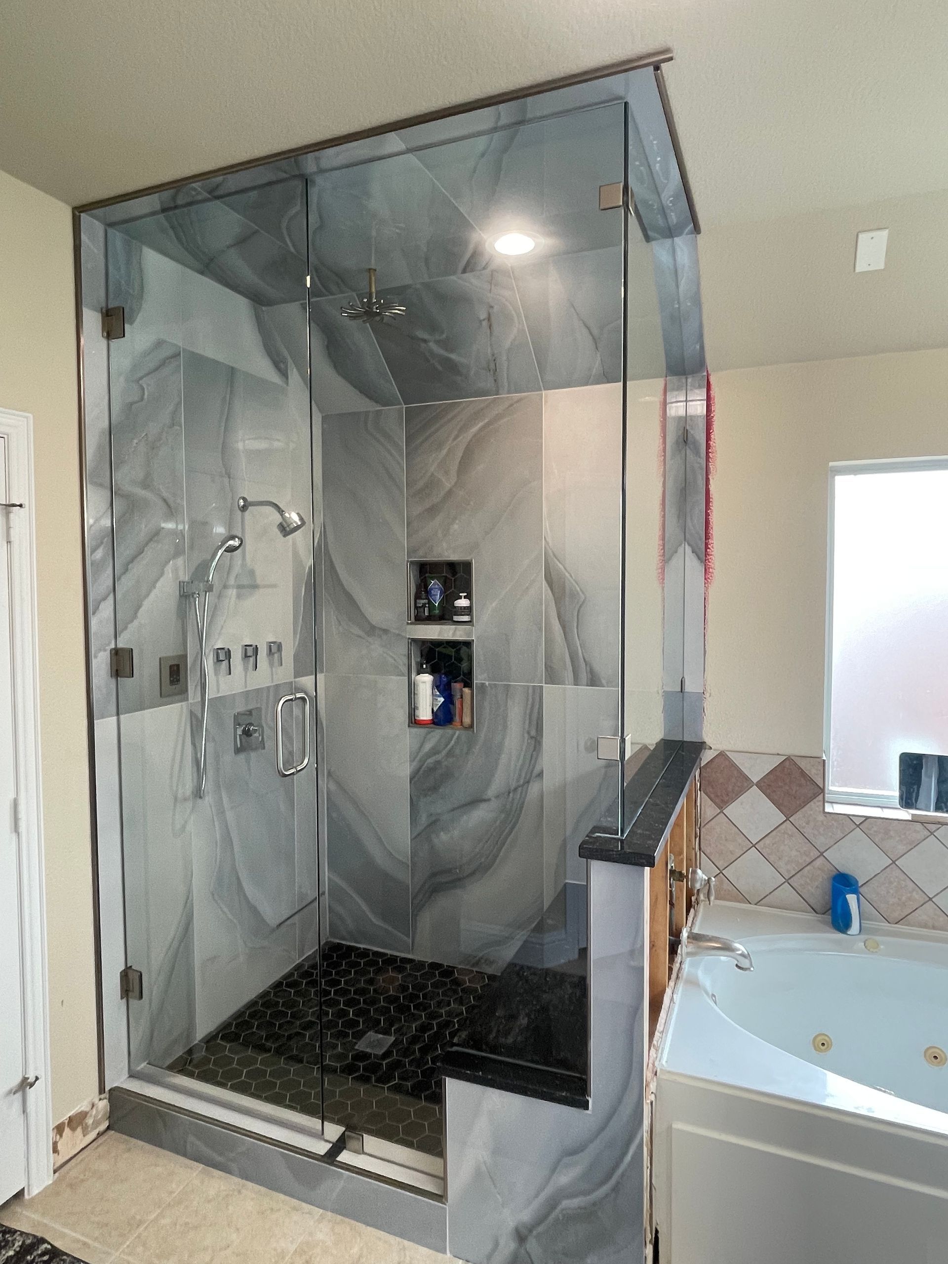 Glass shower enclosure with gray marble tile, black shower floor, and built-in shelves.