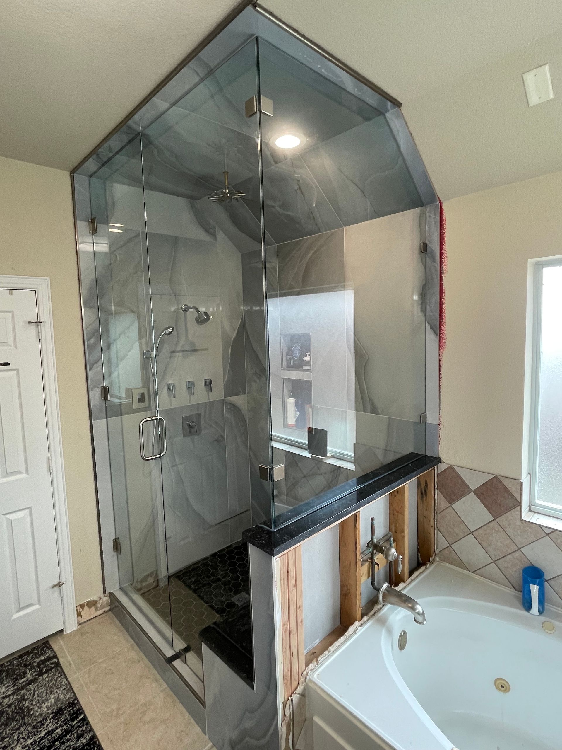Shower with glass walls and a black countertop, next to a bathtub. The walls are partially exposed.