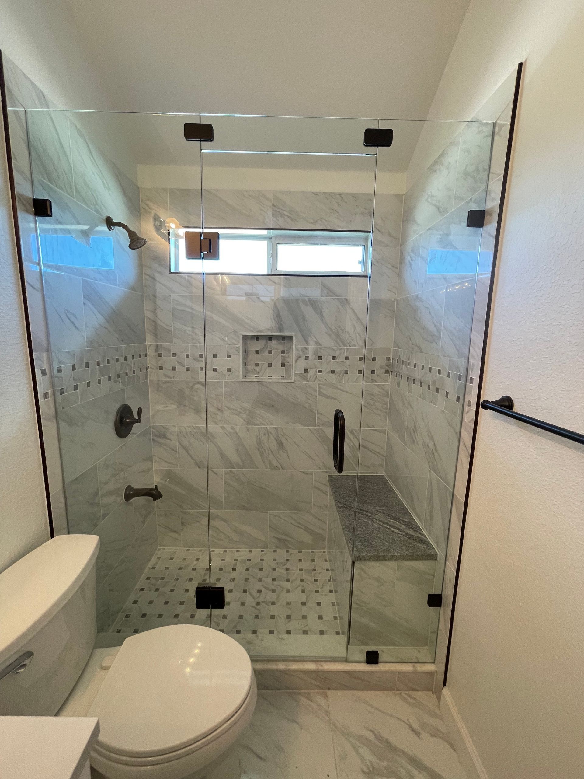 Glass shower enclosure with black hardware and marble tile. Toilet visible.