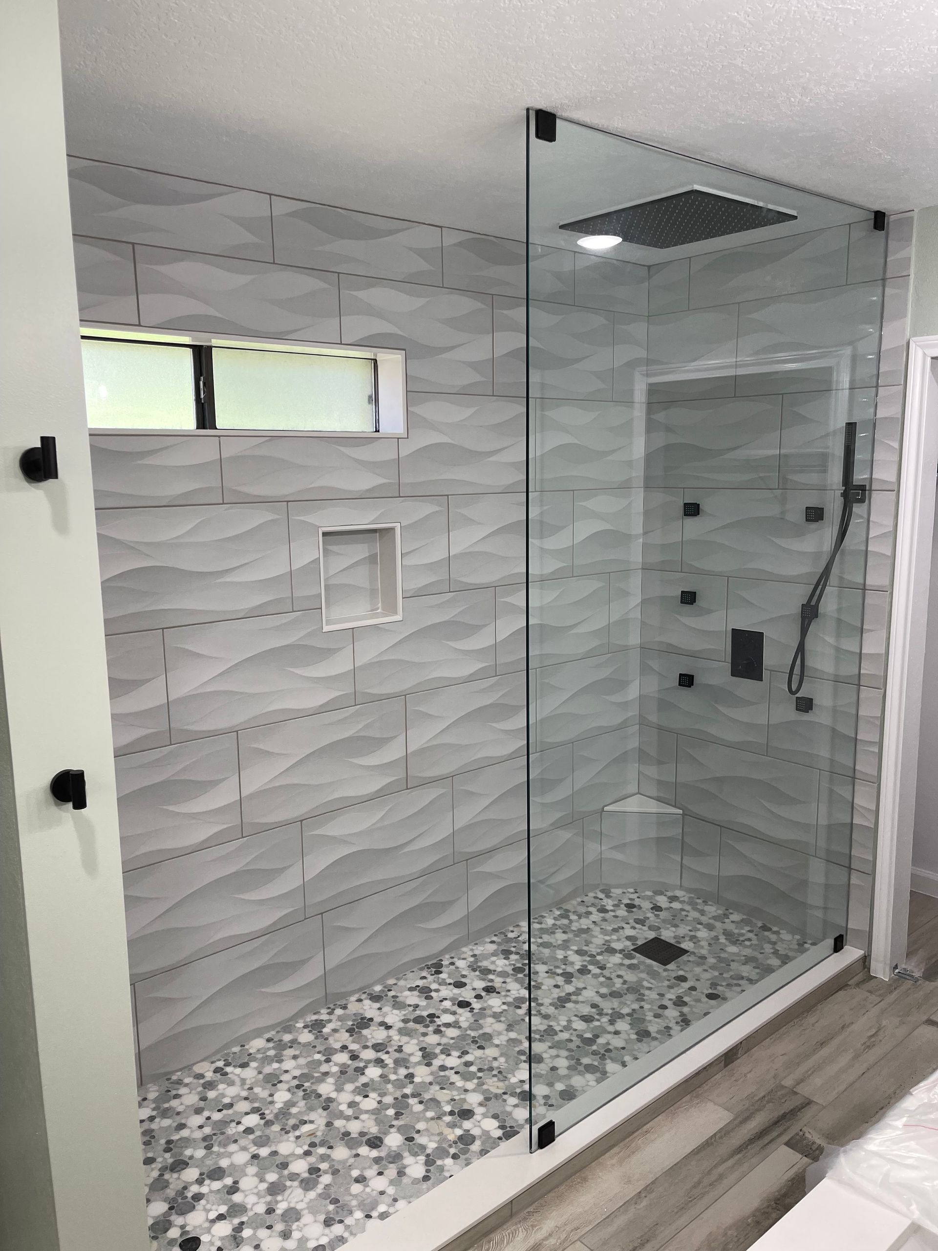 Modern bathroom shower with glass walls, gray textured tile, pebble floor, and rain showerhead.