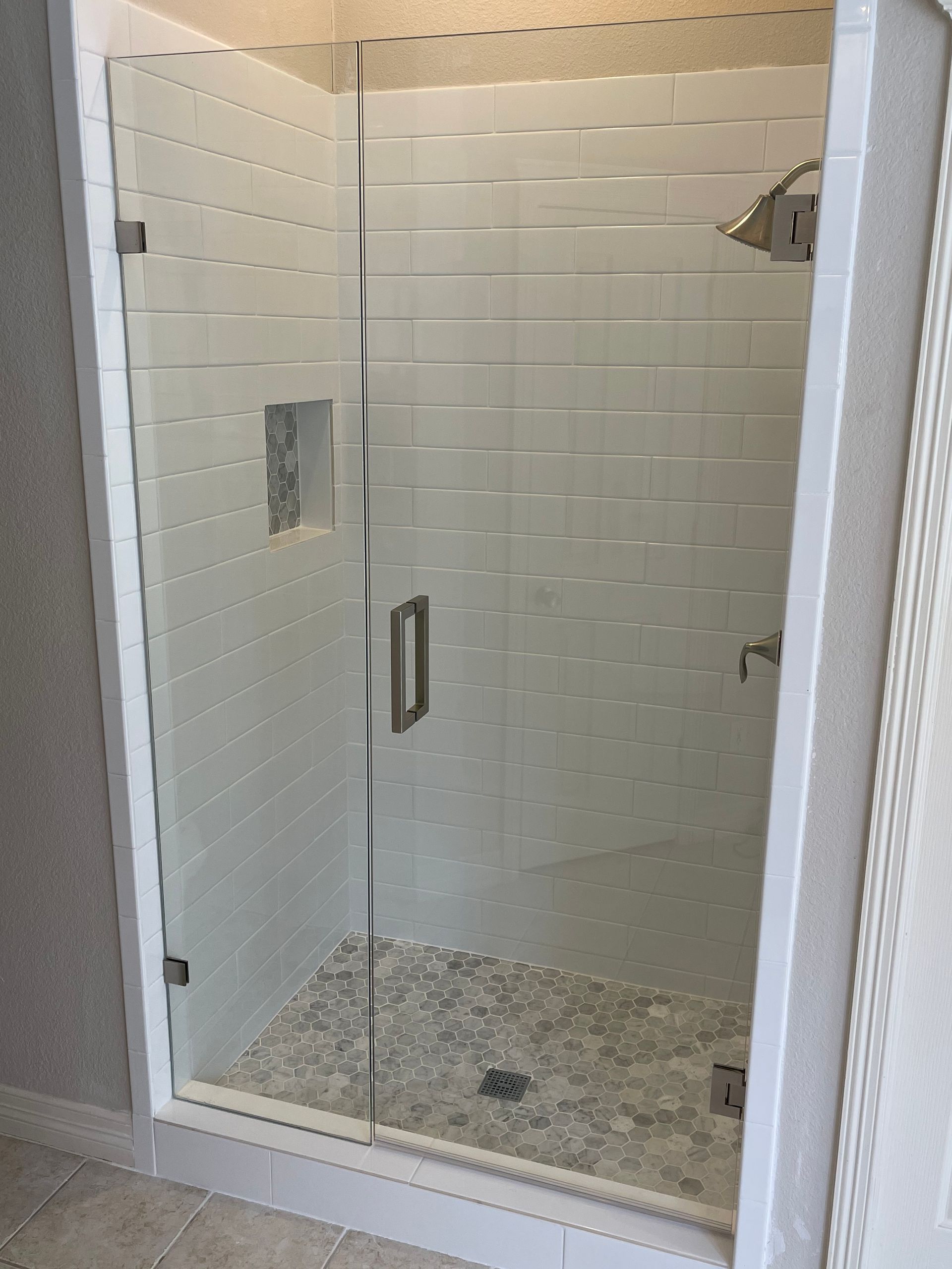 Glass shower enclosure with gray pebbled floor and white tiled walls.