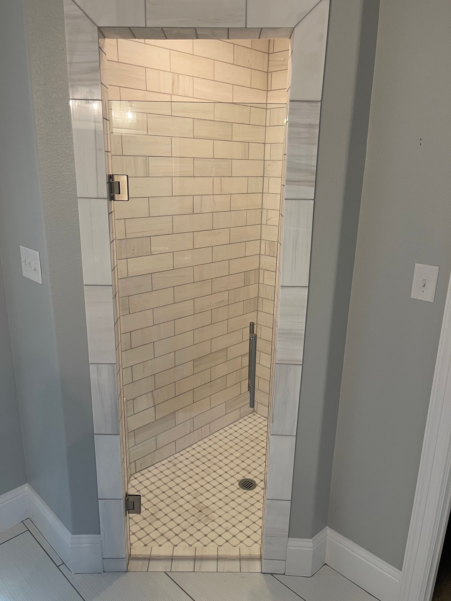 Bathroom shower with white and gray tiled walls and floor, framed by white trim.