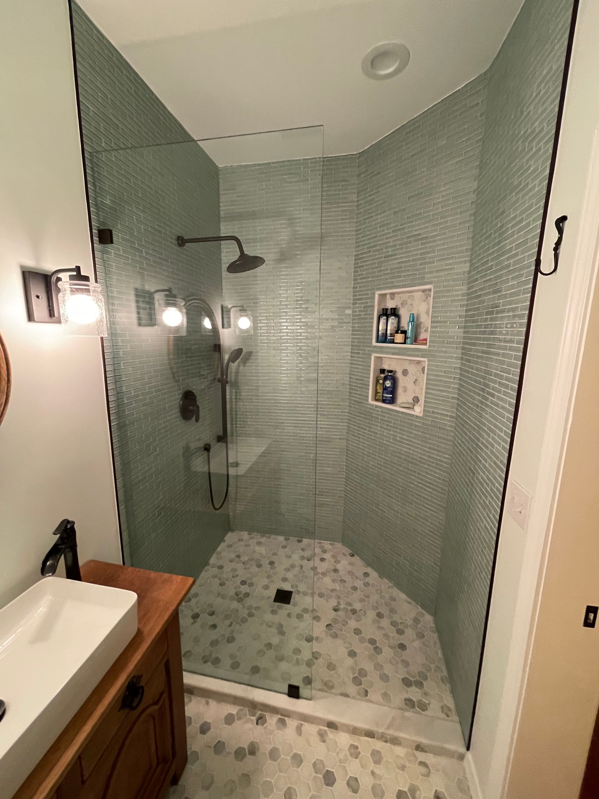 Bathroom with a glass-enclosed shower, green tiled walls, and a stone pebble floor.