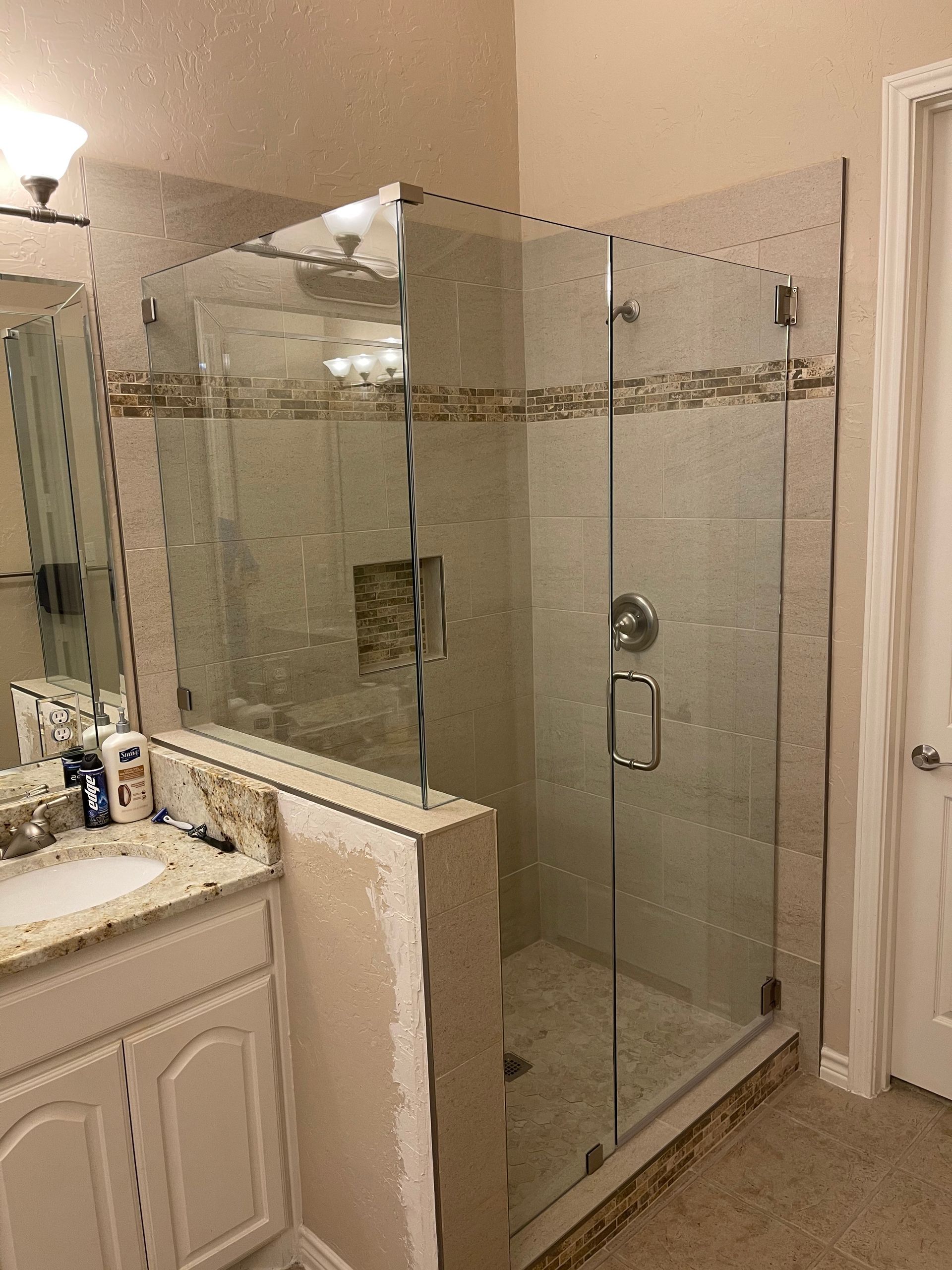 Modern bathroom with glass shower enclosure, tan tile walls, and a white vanity.