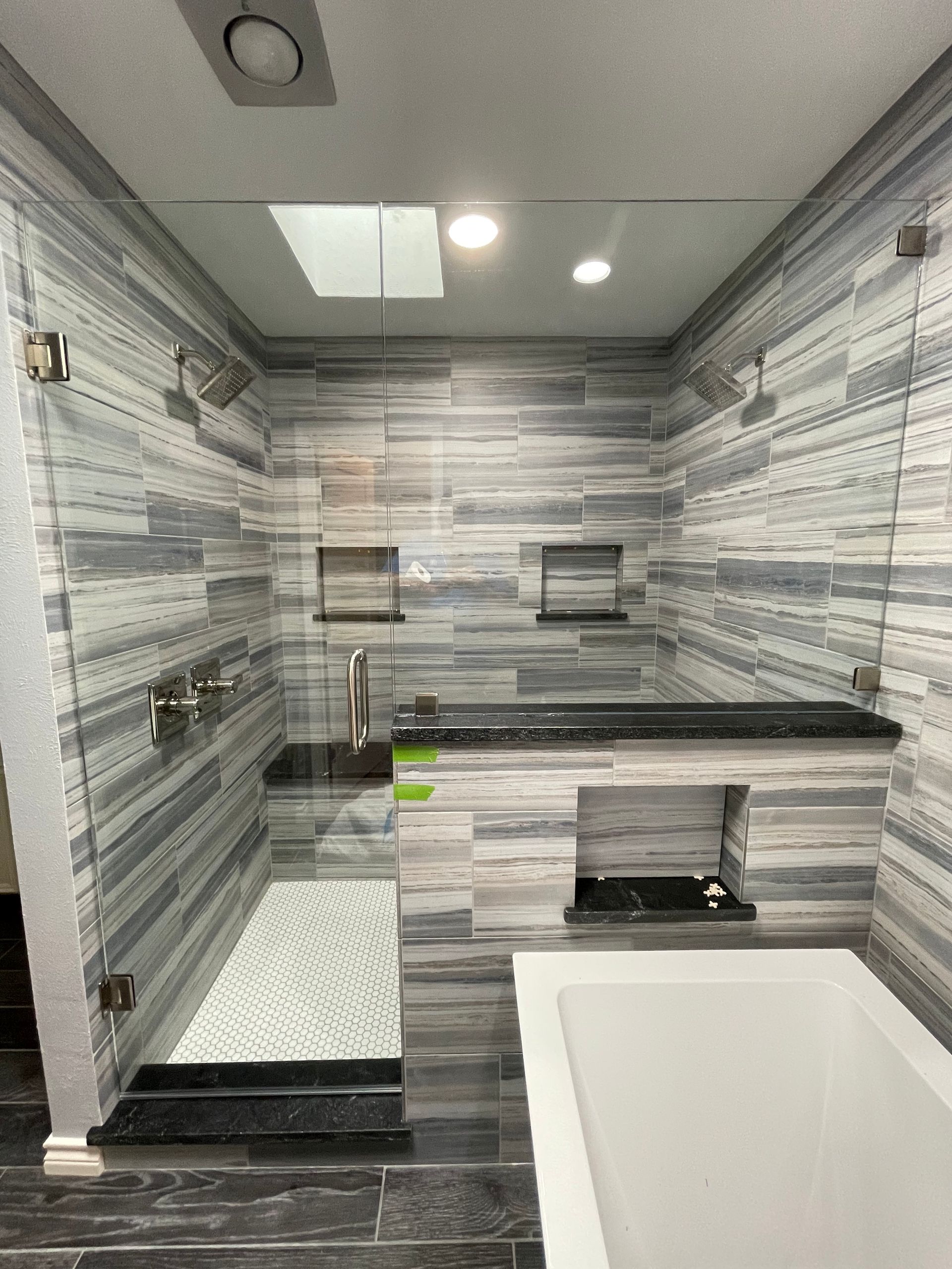 Bathroom with glass shower doors, gray and blue tiled walls, and a built-in bench.