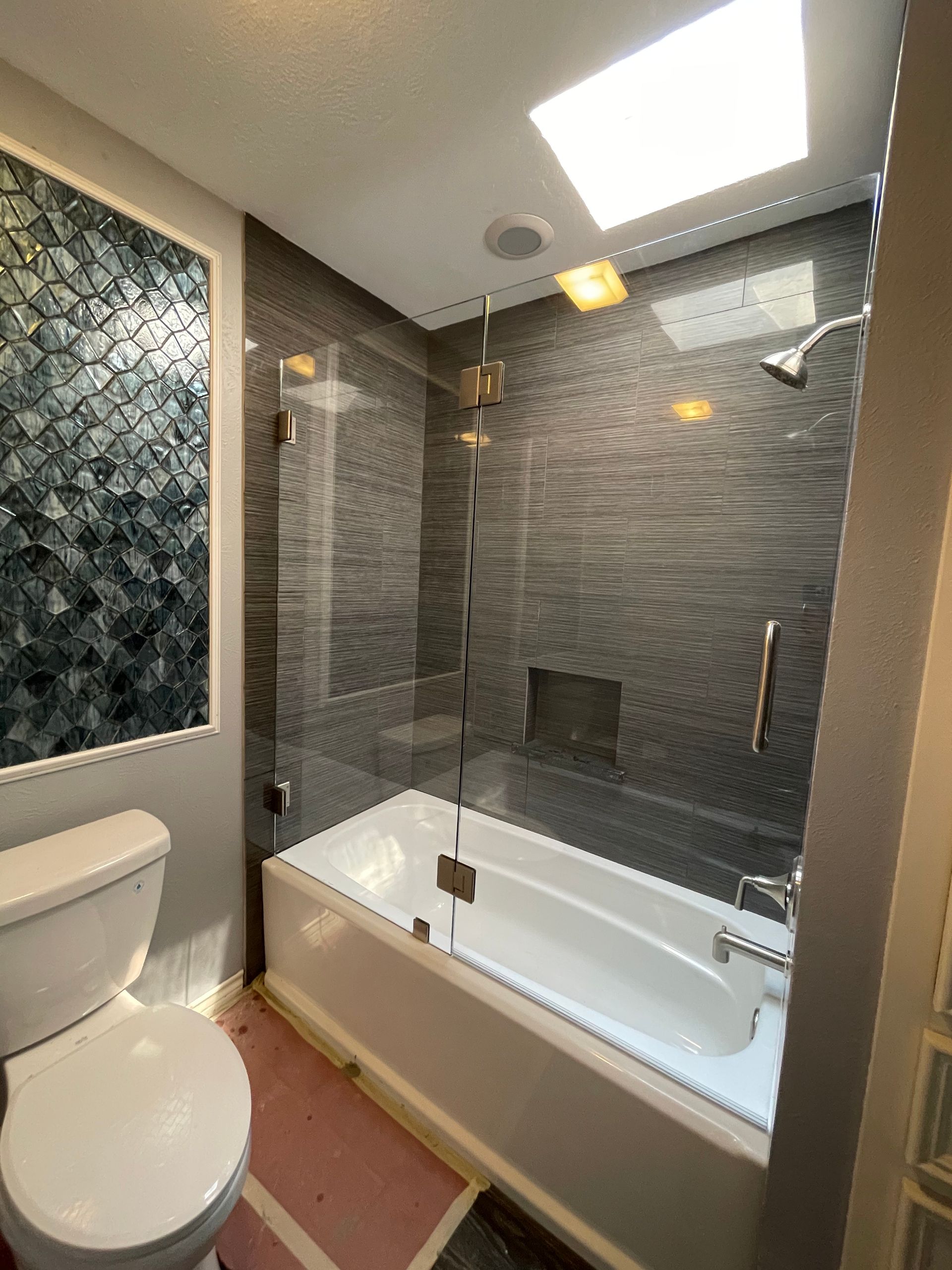 Bathroom with glass shower enclosure, bathtub, and blue-gray mosaic tile.