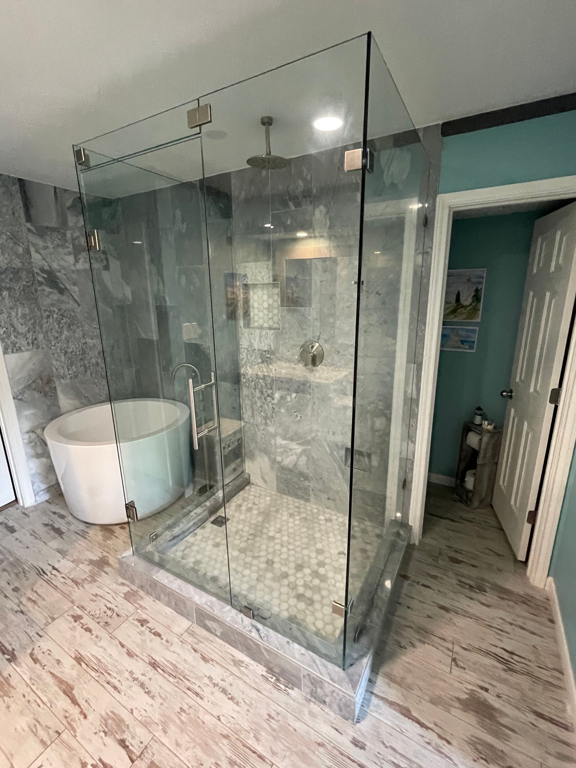 Spacious modern bathroom with glass shower, soaking tub, and stone tile walls.