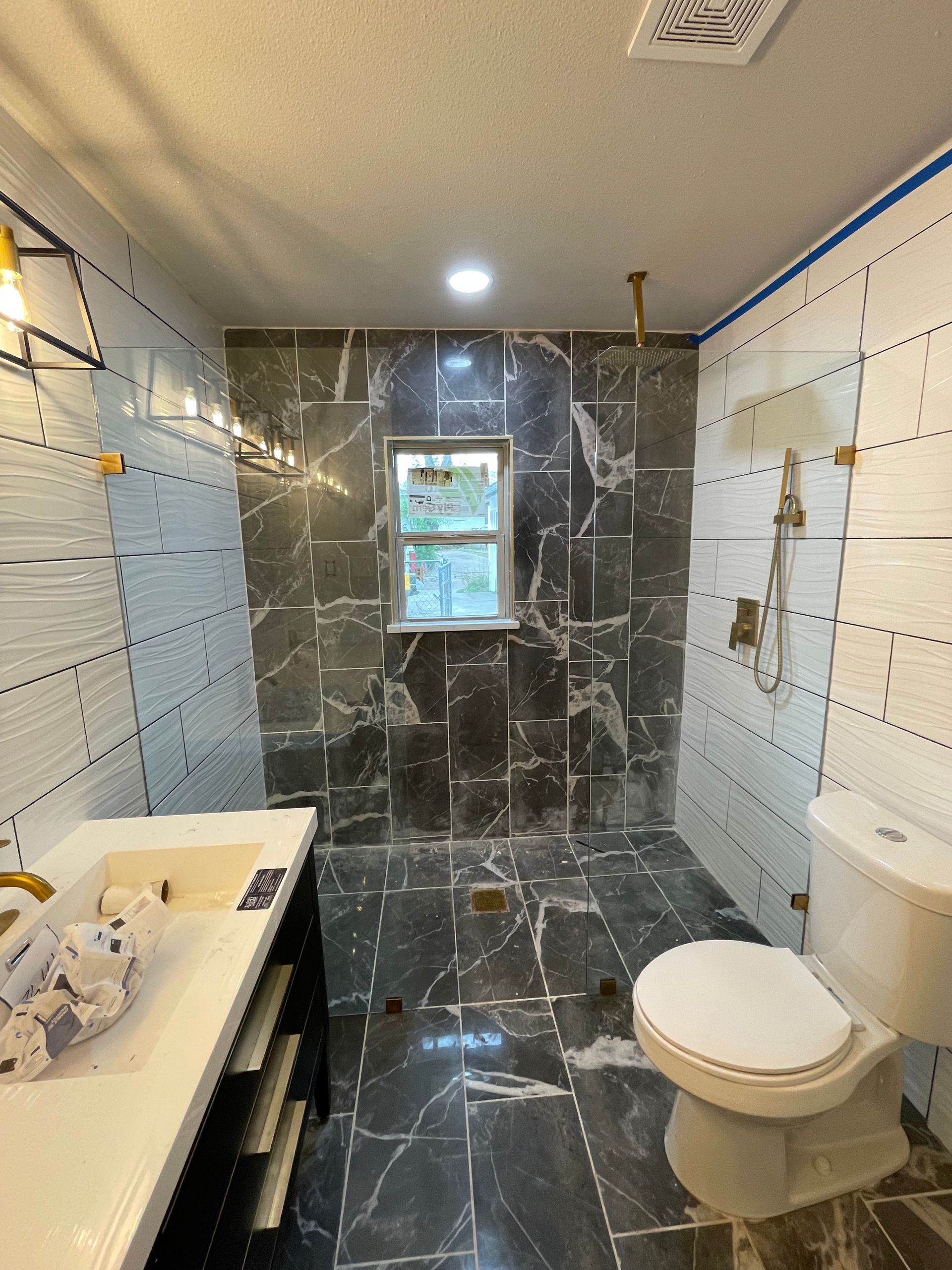 Bathroom renovation: gray marbled shower walls, white tiled side walls, gold fixtures, white toilet, vanity.