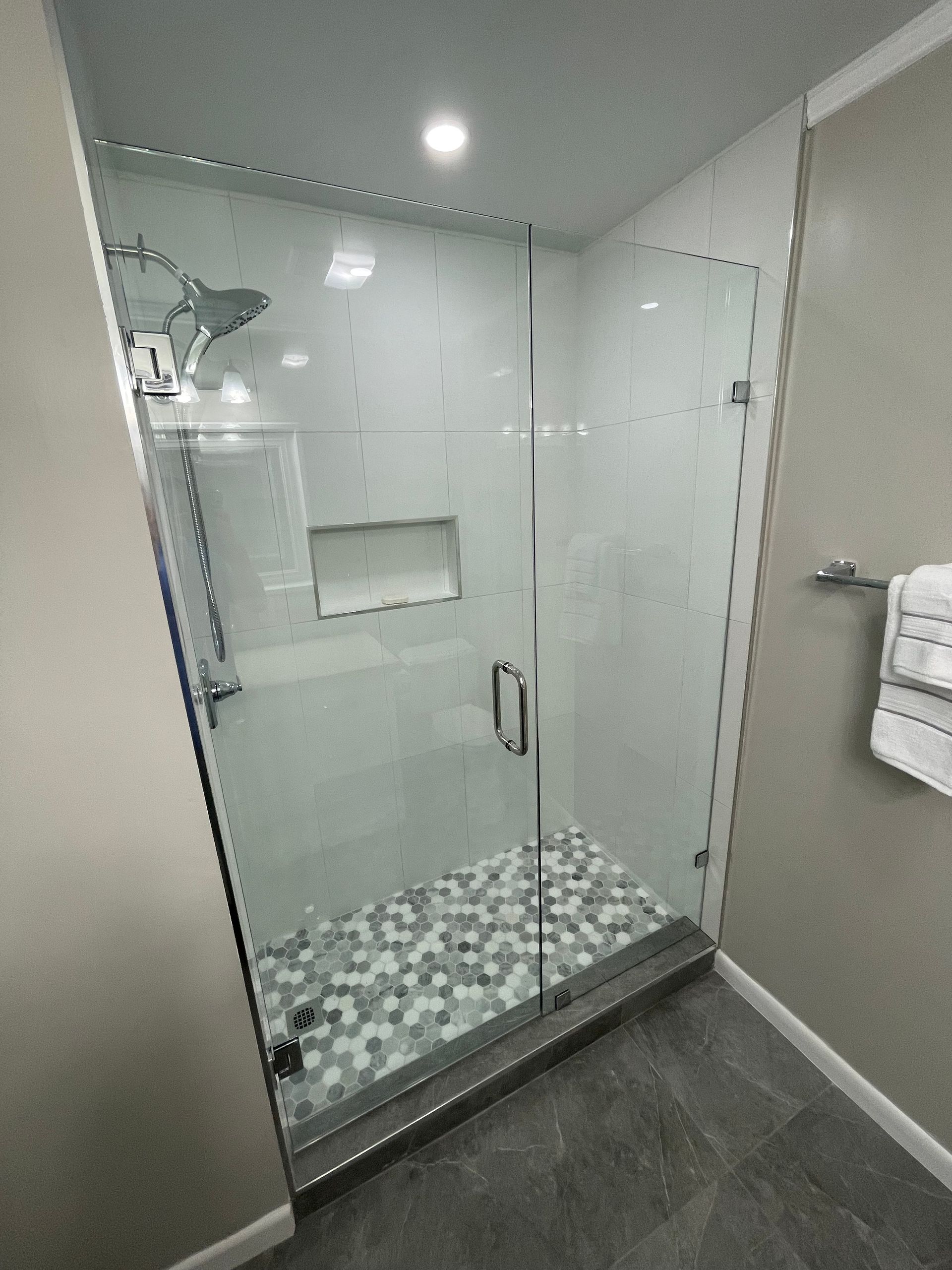 Modern shower with glass door and pebble tile floor. White walls, silver fixtures, towel rack.