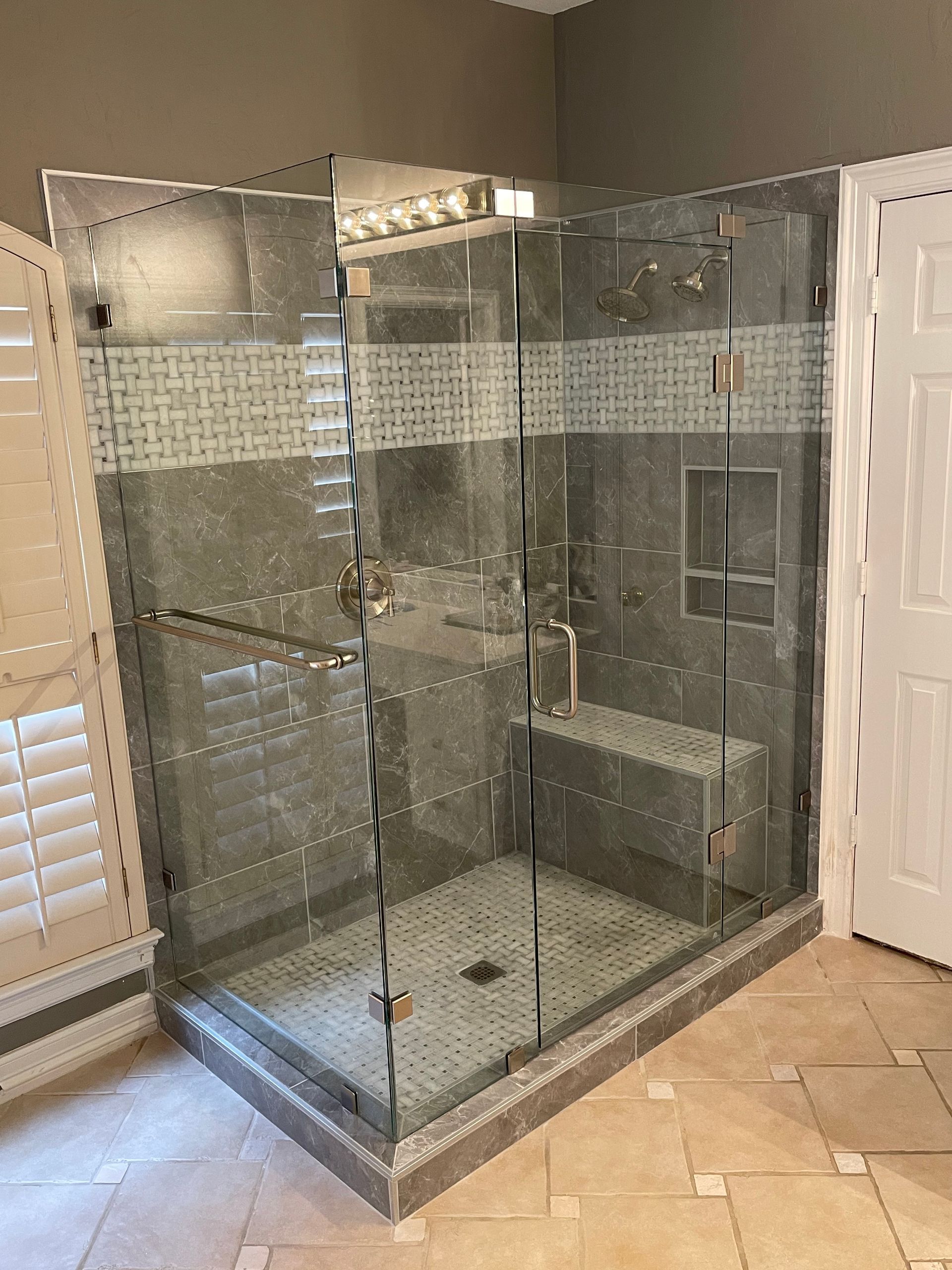 Glass-enclosed shower with dark gray tile and bench, beige floor. Door to right.
