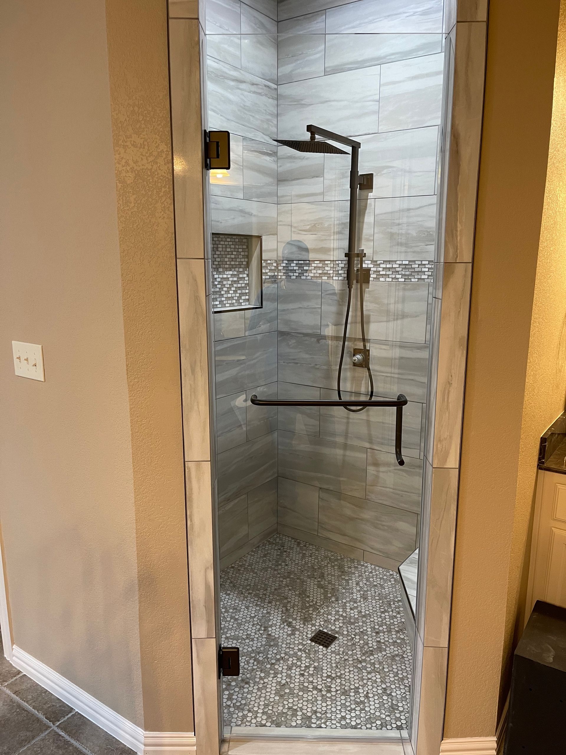 Shower niche with gray tiled walls, stone floor, and glass door. Dark metal fixtures.
