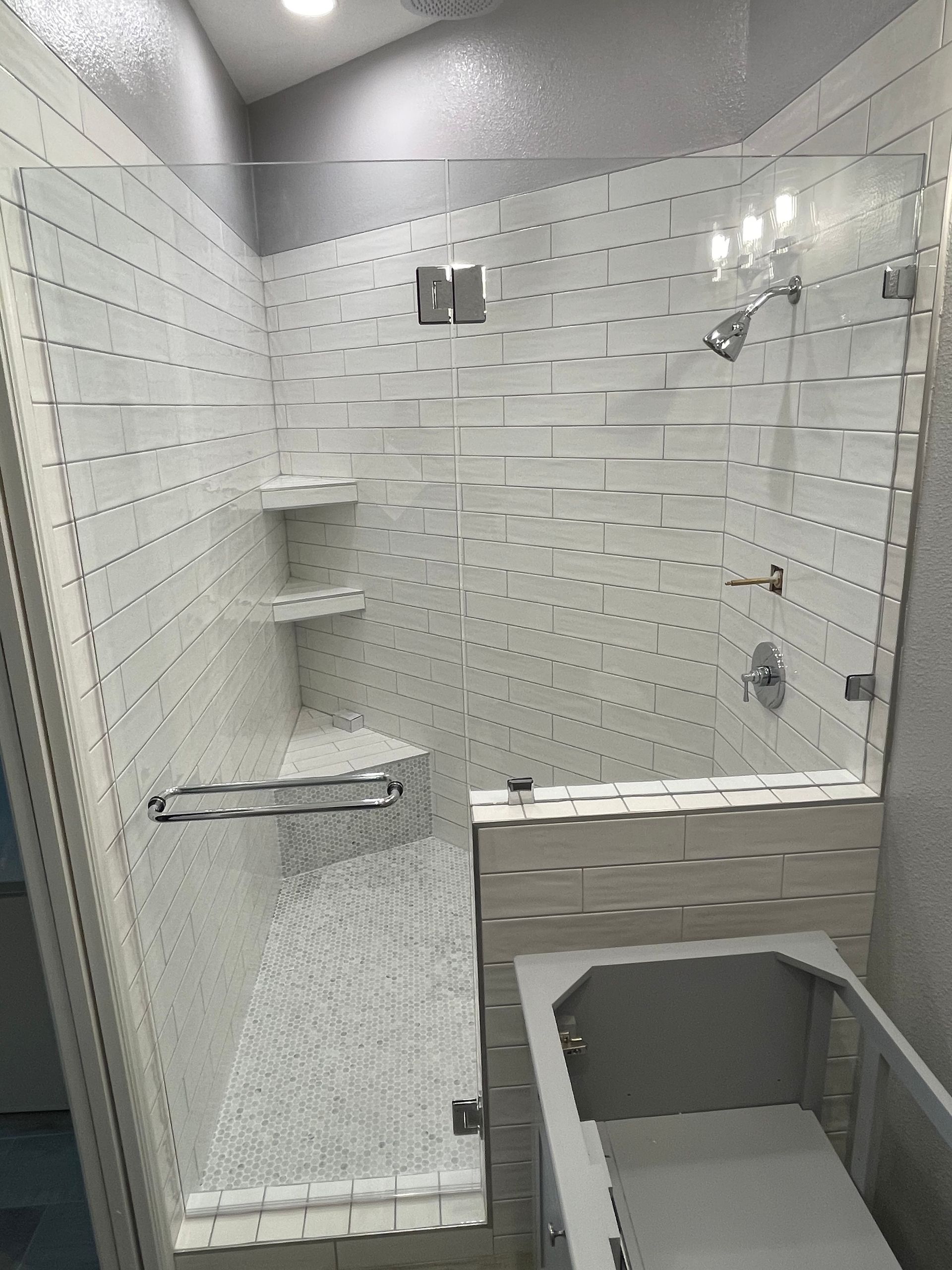 Modern white tiled shower with glass door and built-in shelves; a bathtub is adjacent.