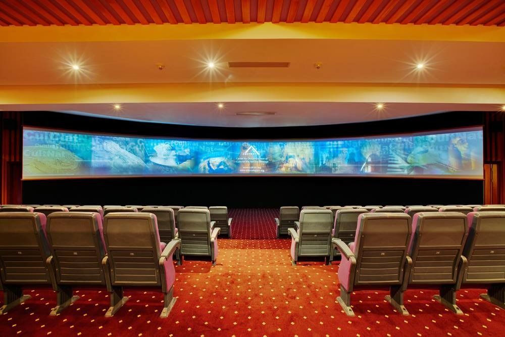 A movie theater with a curved screen and rows of seats, red carpet.